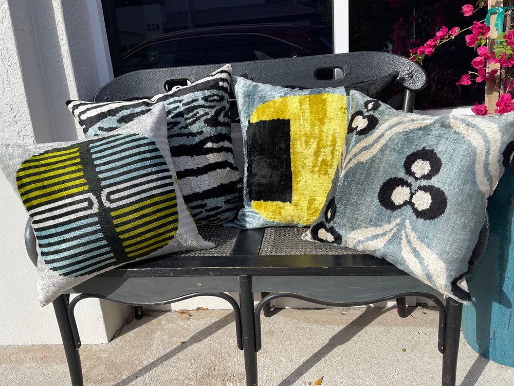 Material World collection of cool-tone artisan throw pillows arranged on a black bench, promoting fair-trade home décor at materialworld.design