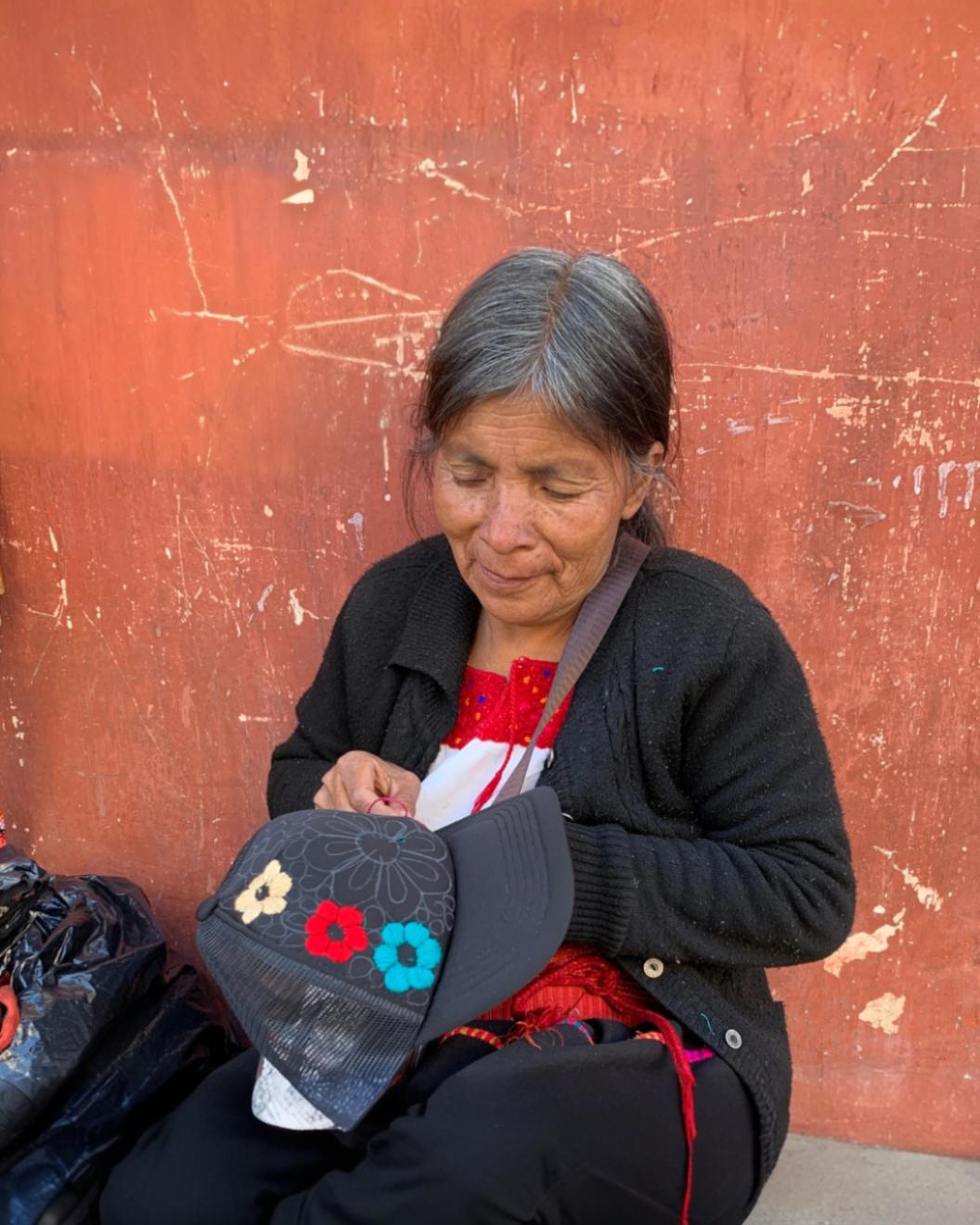 Female artisan hand-embroidering a black cap with colorful floral designs